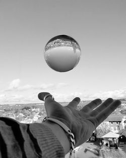 Cropped hand throwing crystal ball against sky