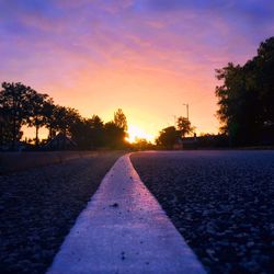 Road by silhouette trees against sky during sunset