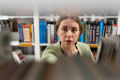 Middle-aged female choose book from bookshelf in college, university library for education research