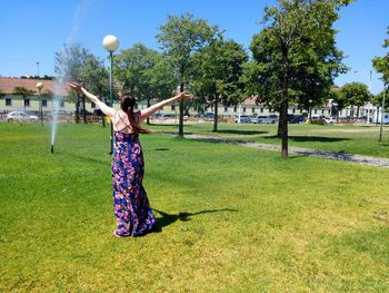 Rear view full length of woman with arms outstretched on grassy field