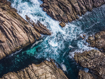 High angle view of waves splashing on rock formations at beach