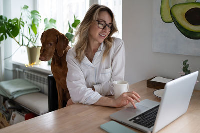 Woman with dog using laptop on table