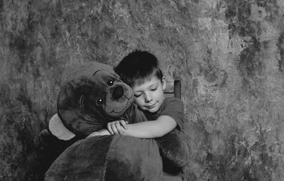 Boy embracing teddy bear against wall