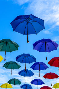 Low angle view of umbrellas levitating against blue sky
