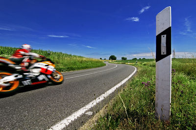 Road amidst grass against blue sky