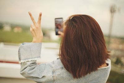 Woman gesturing peace sign while taking selfie