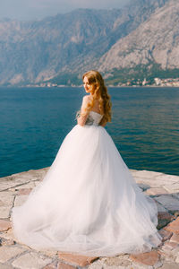 Woman standing on rock by sea against mountain