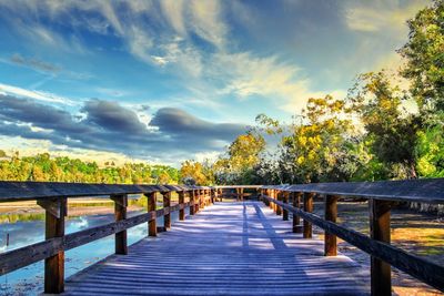 Wooden footbridge along trees and plants against sky