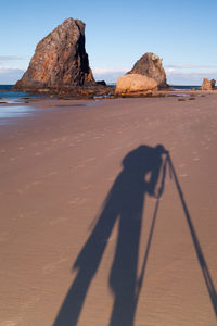 Shadow of man on rock at beach against sky