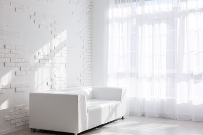 Bright, minimalist living room interior with white sofa standing near the window and black stool