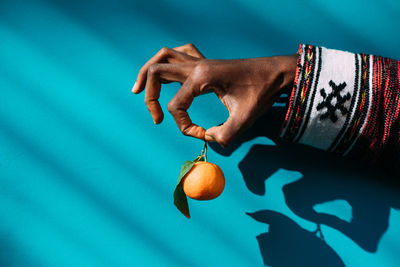 Cropped hand holding orange against wall