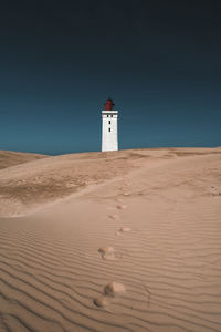 Lighthouse on sand dune against sky