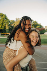 Portrait of happy teenage girl giving piggyback ride to cheerful friend at park