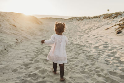 Behind view of young girl walking away at beach during sunset