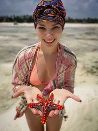 Portrait of smiling young woman holding starfish at beach