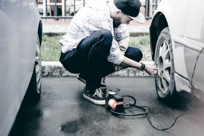 Young man inflating car tire with air pump at parking lot