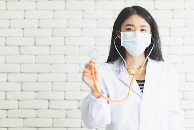 Portrait of doctor holding stethoscope against white wall