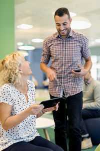 Happy businesspeople with technologies conversing at office lobby