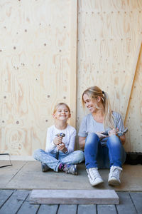 Happy mother and daughter holding hammers against wall of house being renovated