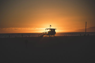 Silhouette hut on beach against sky during sunset