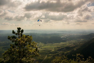 Person paragliding over landscape against cloudy sky