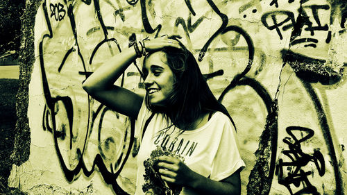 Cheerful woman with hand in hair against graffiti on wall