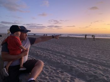 People at beach against sky during sunset