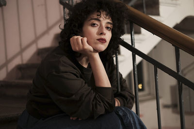 Portrait of woman with curly hair sitting on steps at home