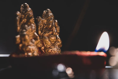 Close-up of figurines by lit oil lamp in darkroom