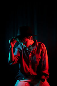 Young woman wearing hat sitting against black background