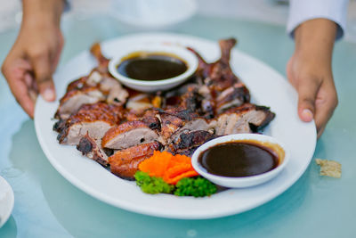 Cropped hands of woman holding food in plate at table