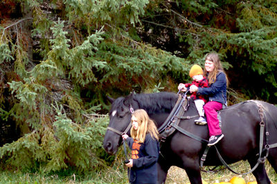 Young woman holding horse while siblings riding