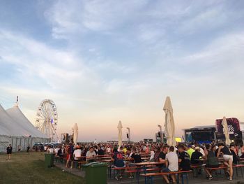 People enjoying at amusement park against sky during sunset