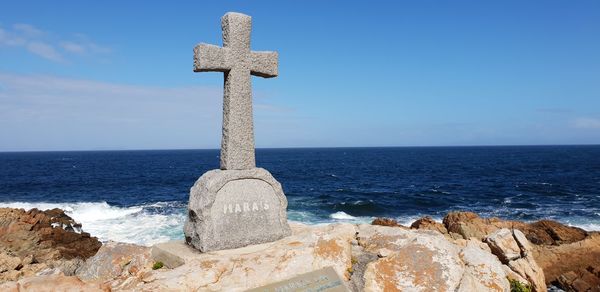 Cross on rock by sea against blue sky
