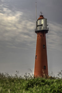 Lighthouse on field by building against sky