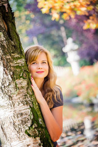 Young woman hiding behind the tree in autumn park.