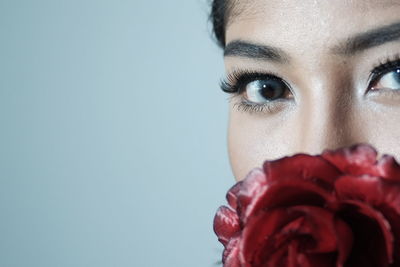 Close-up portrait of beautiful woman with red rose against blue background