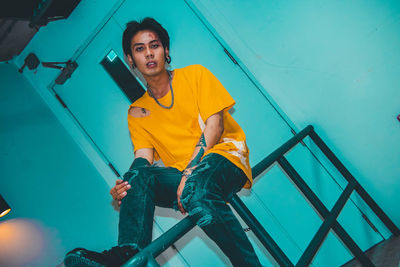 Portrait of young man sitting on railing against wall