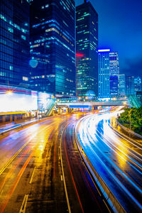 Light trails on city street by illuminated buildings at night