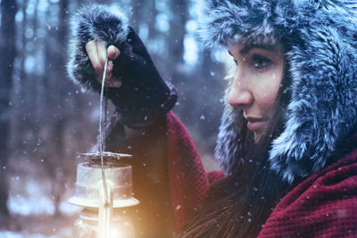 Close-up of young woman holding lantern during snowfall