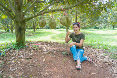 Portrait of woman pointing at fruit hanging on tree