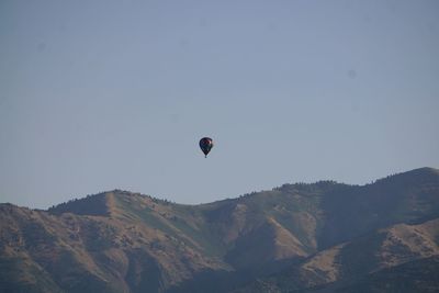 Person paragliding over mountains against clear sky