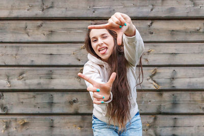 Portrait of young woman with arms raised standing against wall