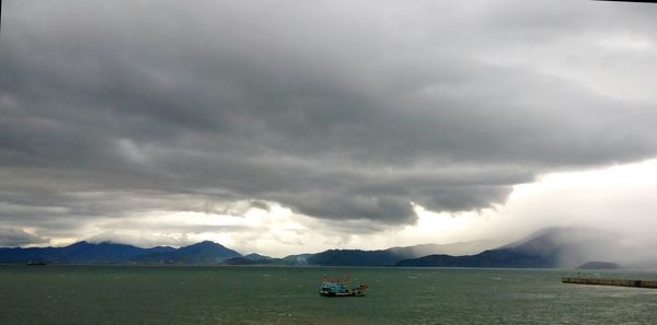 Boat sailing in sea against cloudy sky