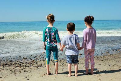 Rear view of siblings standing at beach against sky