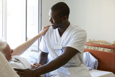 Smiling male nurse consoling senior man in hospital ward