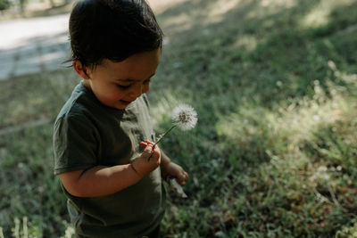 Rear view of boy looking at dandelion