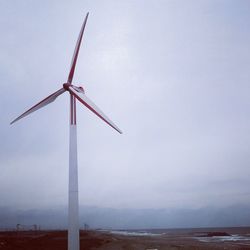 Low angle view of wind turbine by sea against sky