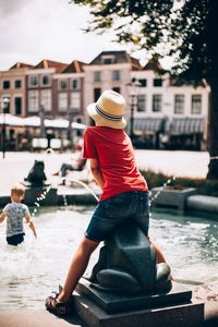 Rear view of man sitting by river in city