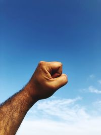 Cropped hand of man gesturing fist against blue sky